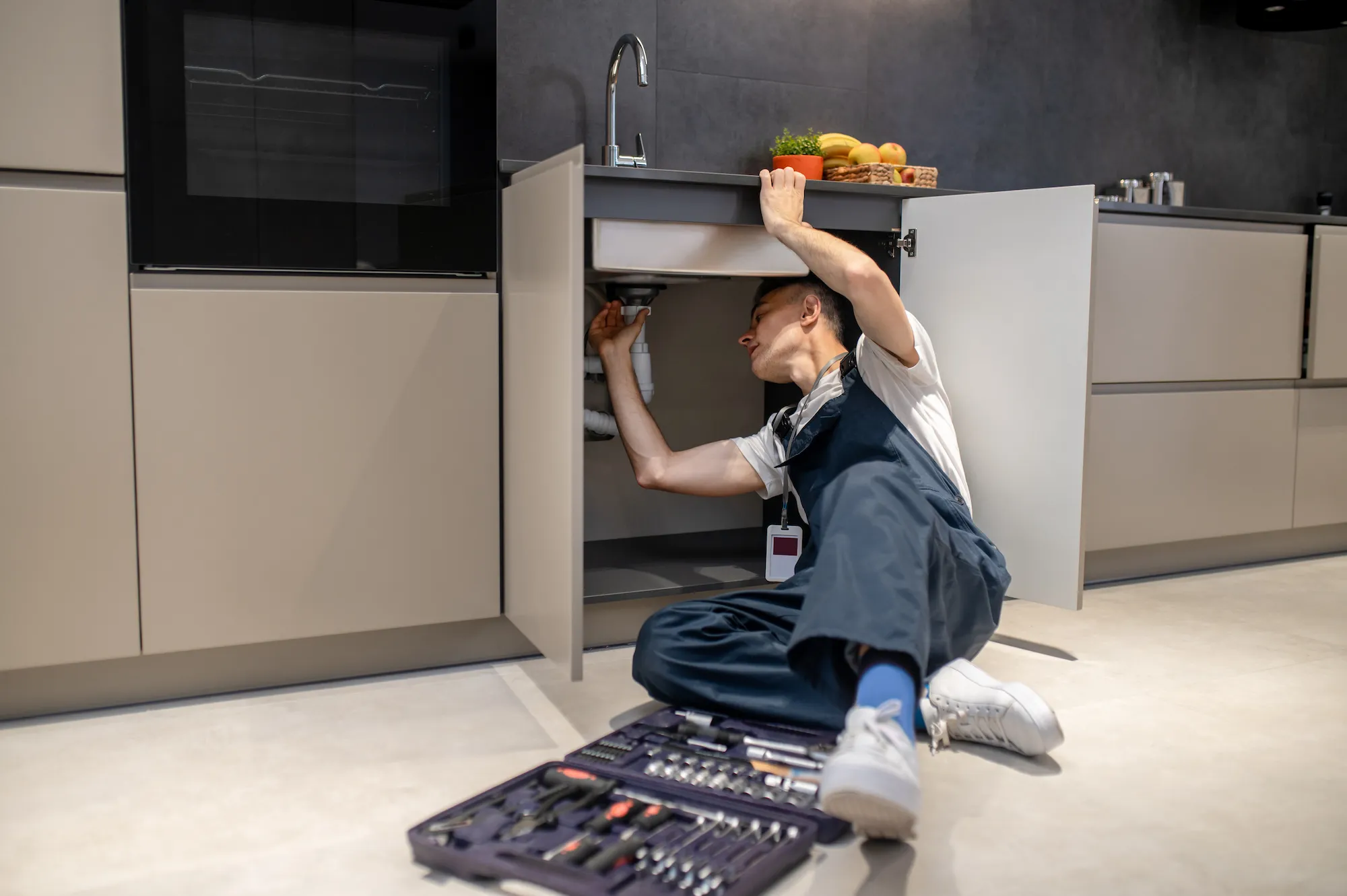 household repair middle aged man inspecting pipe touching hand under sink in stylish modern kitchen