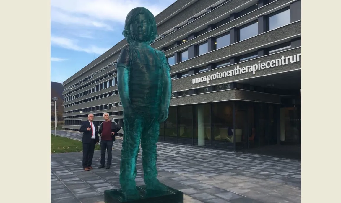 het reuzenkind voor het protonentherapiecentrum van het umcg met daarachter bestuursvoorzitter jos aartsen links en kunstenaar herman lamers e1539451517551