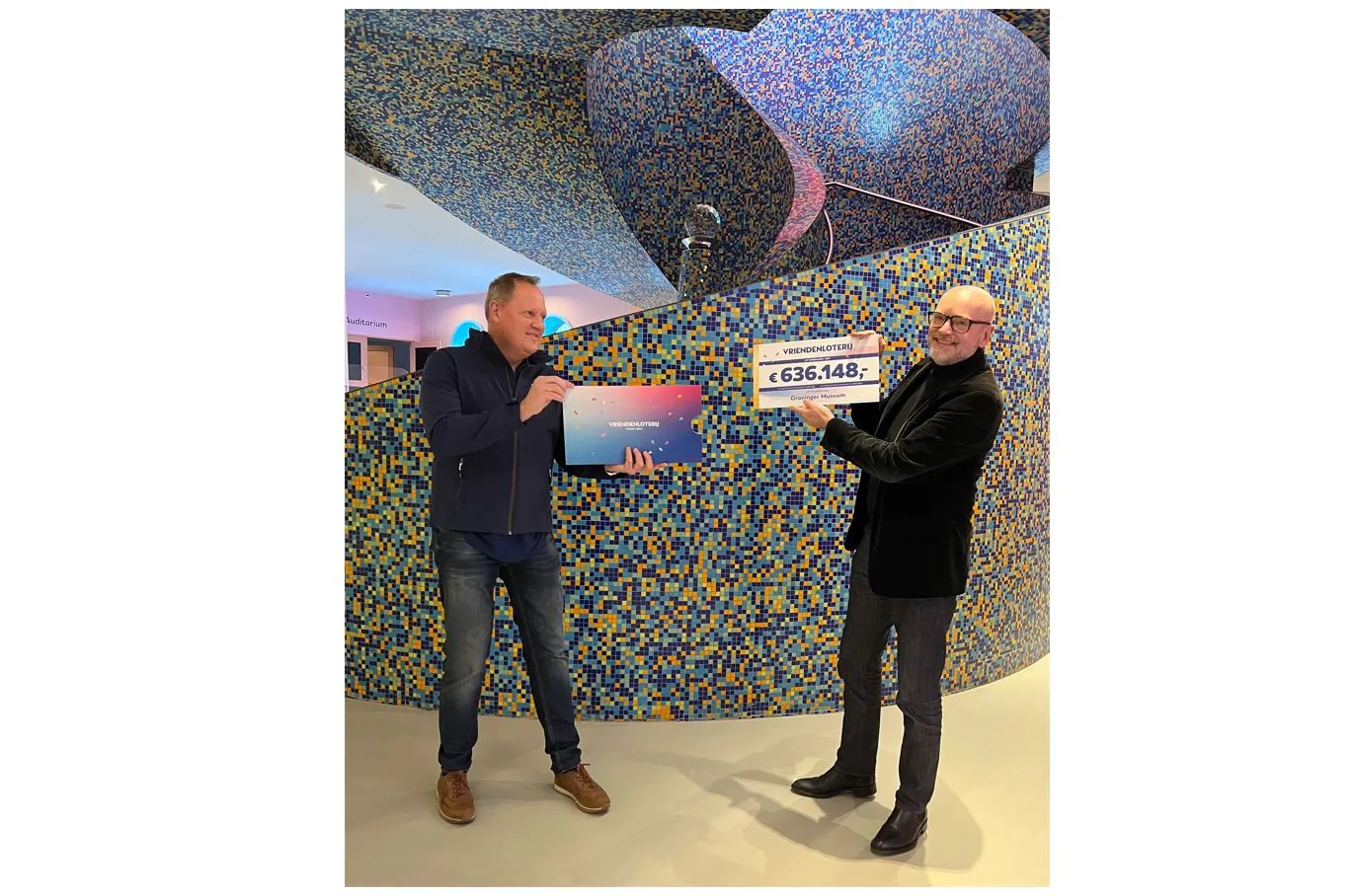 medewerker van de vriendenloterij reikt cheque uit aan andreas bluhm directeur van het groninger museum