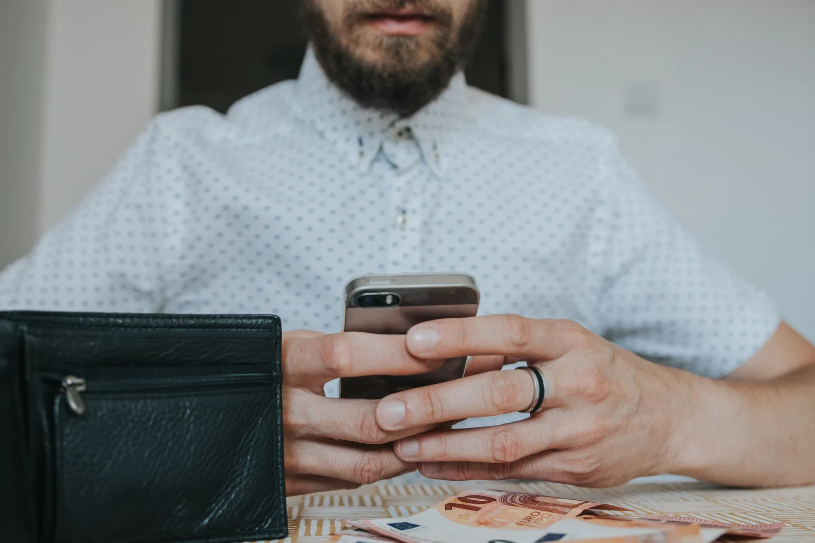 canva person holding silver iphone beside table with black leather wallet and two 10 banknotes 1