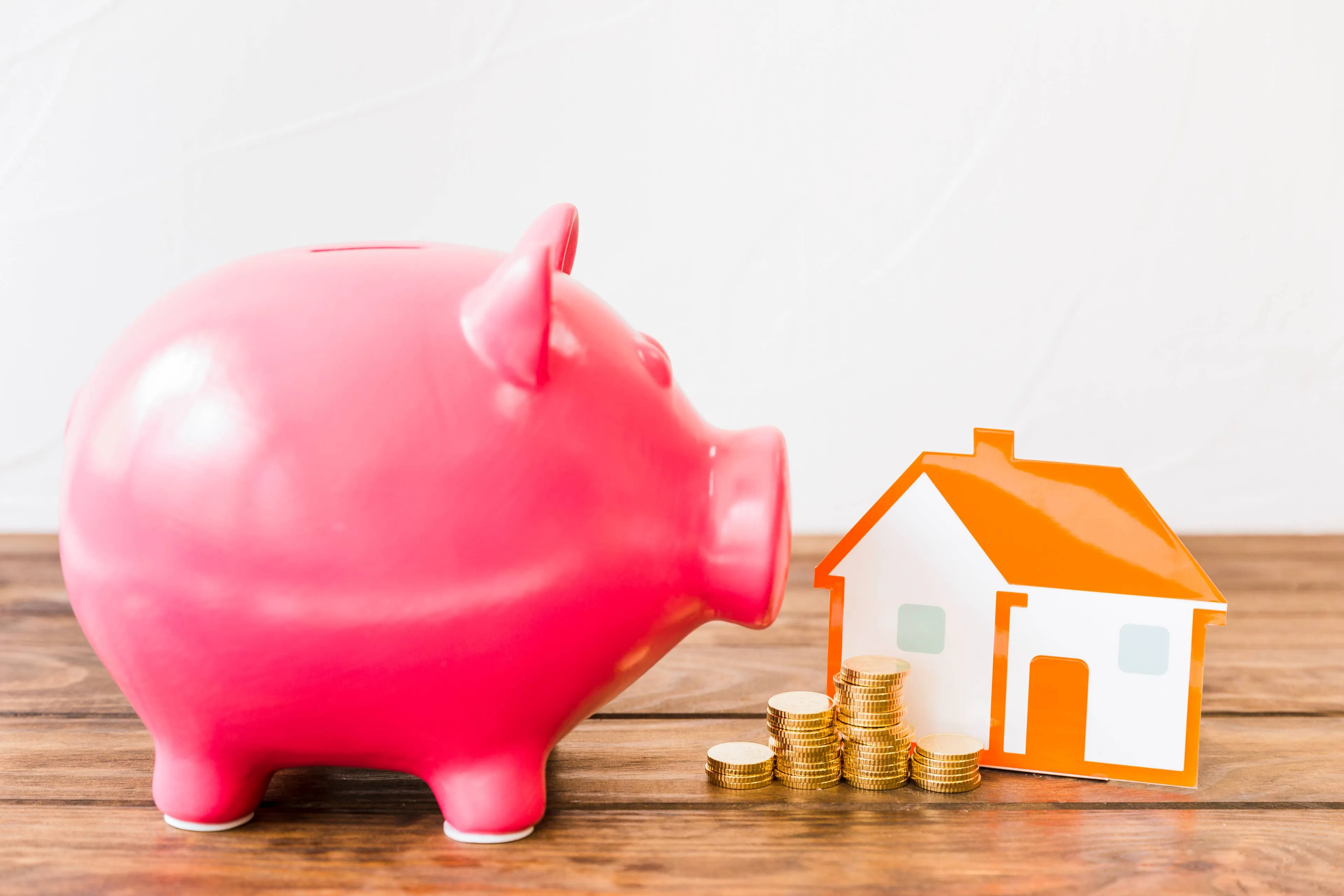 pink-piggybank-near-stacked-coins-house-wooden-desk