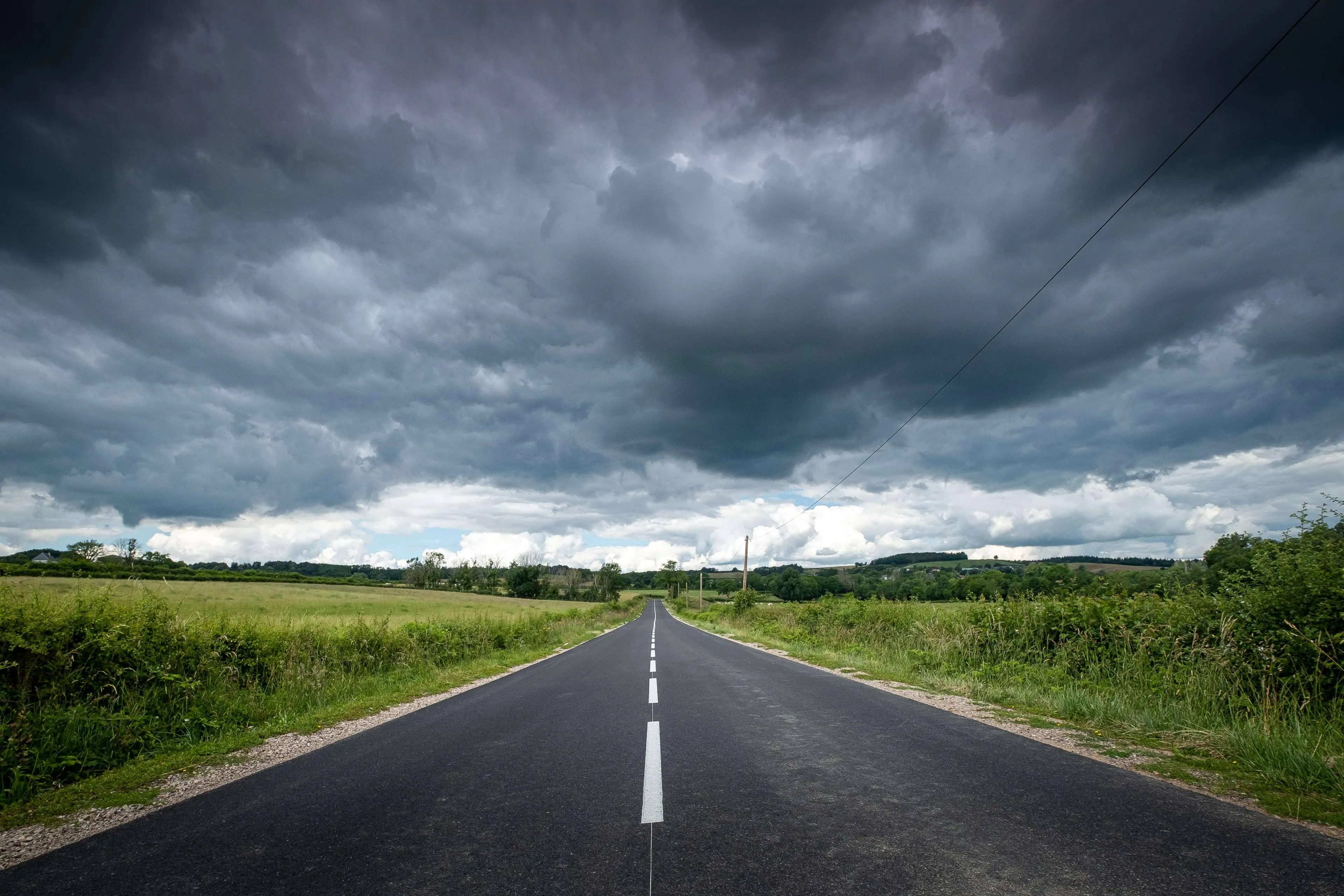 beautiful-view-empty-road-surrounded-by-greenery-dark-storm-clouds
