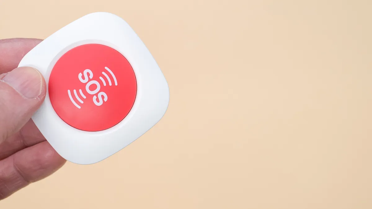 oudere hand met een draadloze sos noodalarmknop geisoleerd op lichtbruine achtergrond