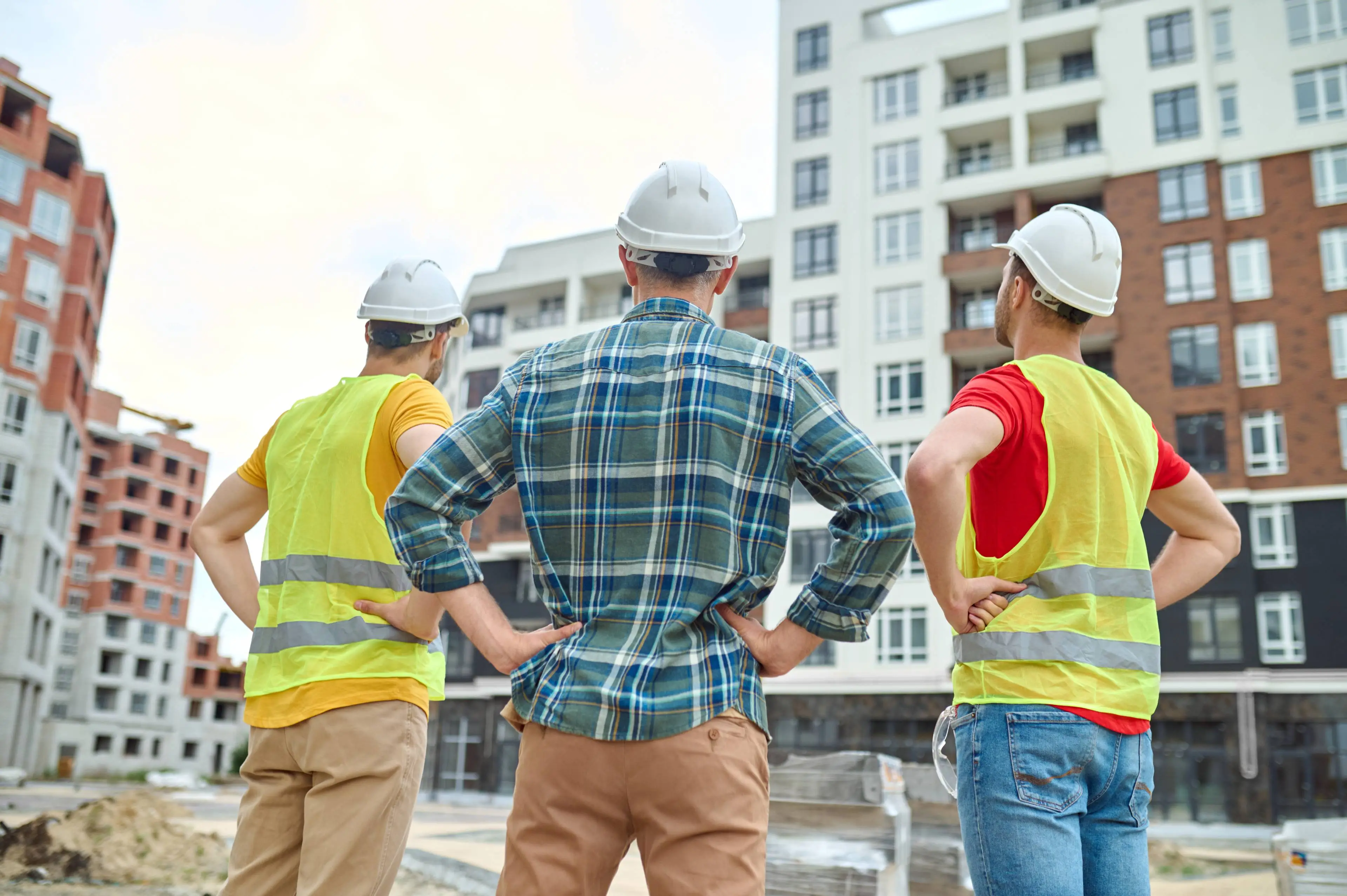 result-back-view-three-men-protective-helmets-holding-hands-his-waist-standing-construction-site-looking-buildings-construction-day