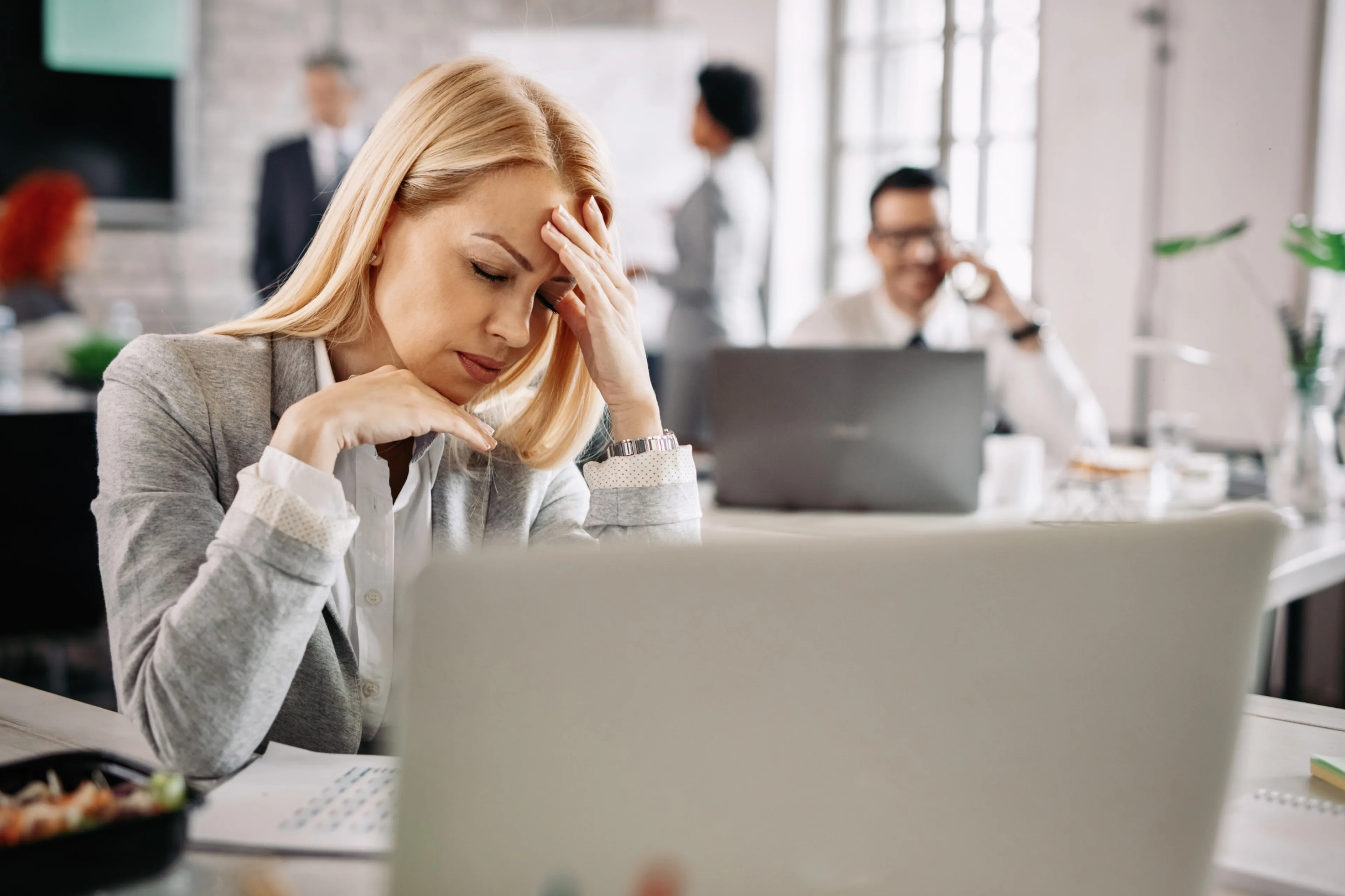 stressed businesswoman holding her head pain having headache work there are people background