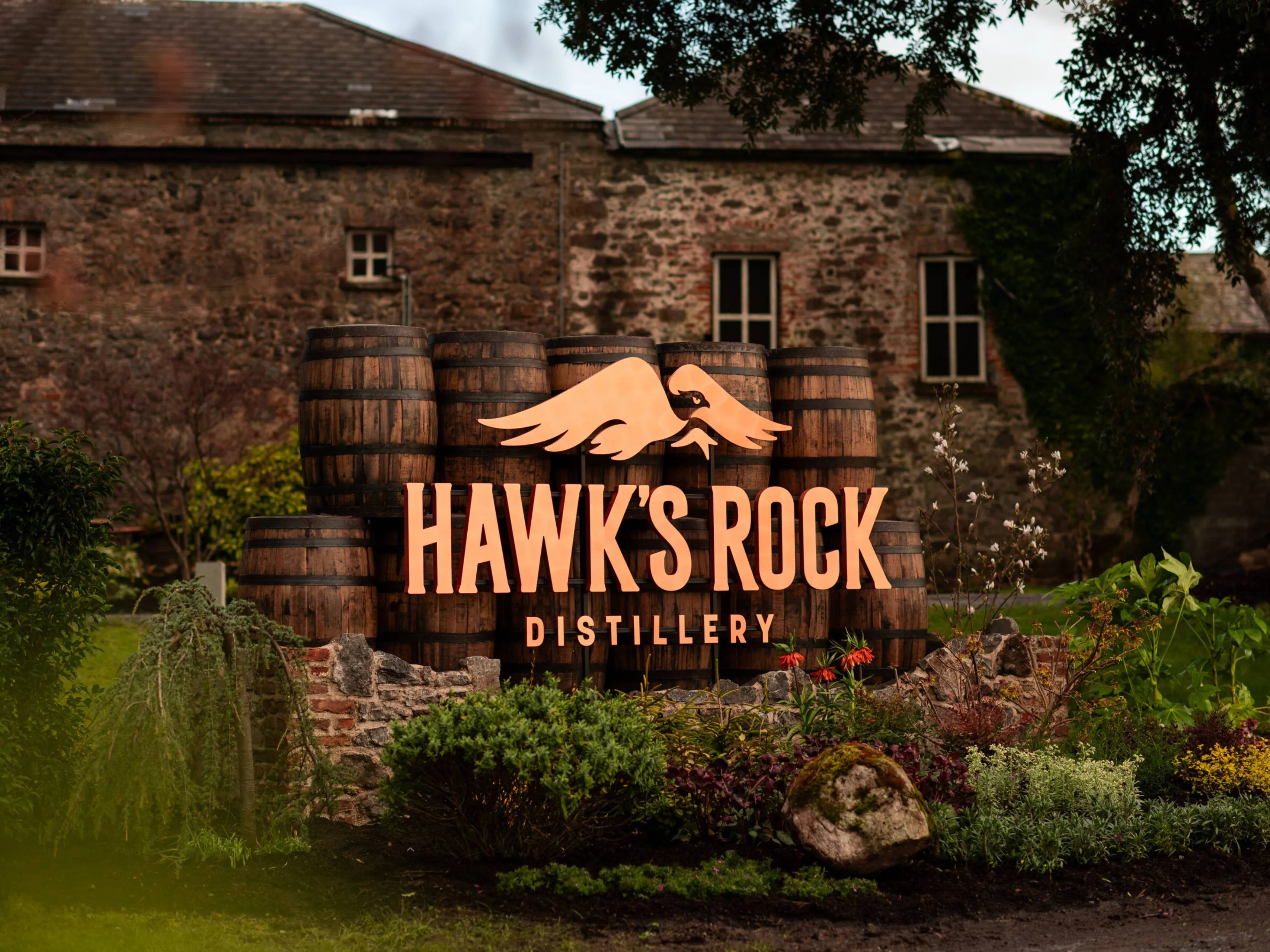 Hawks Rock distilleerderij met vaten op de voorgrond en het logo