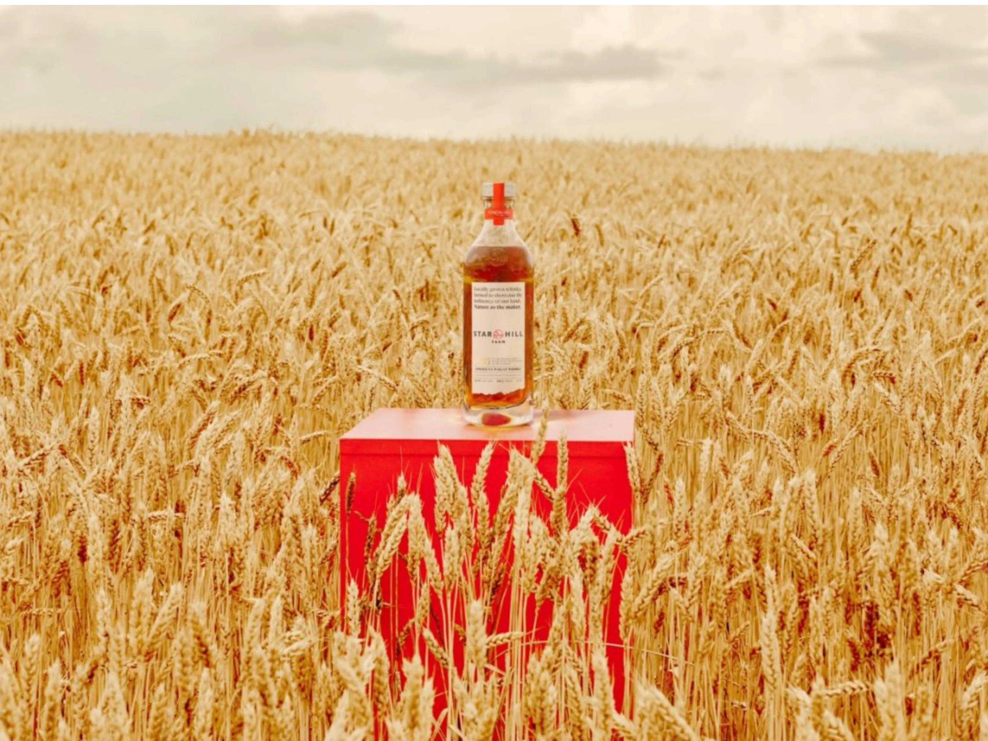 Een fles Star Hill Farm whisky midden in een graanveld op een rode kist