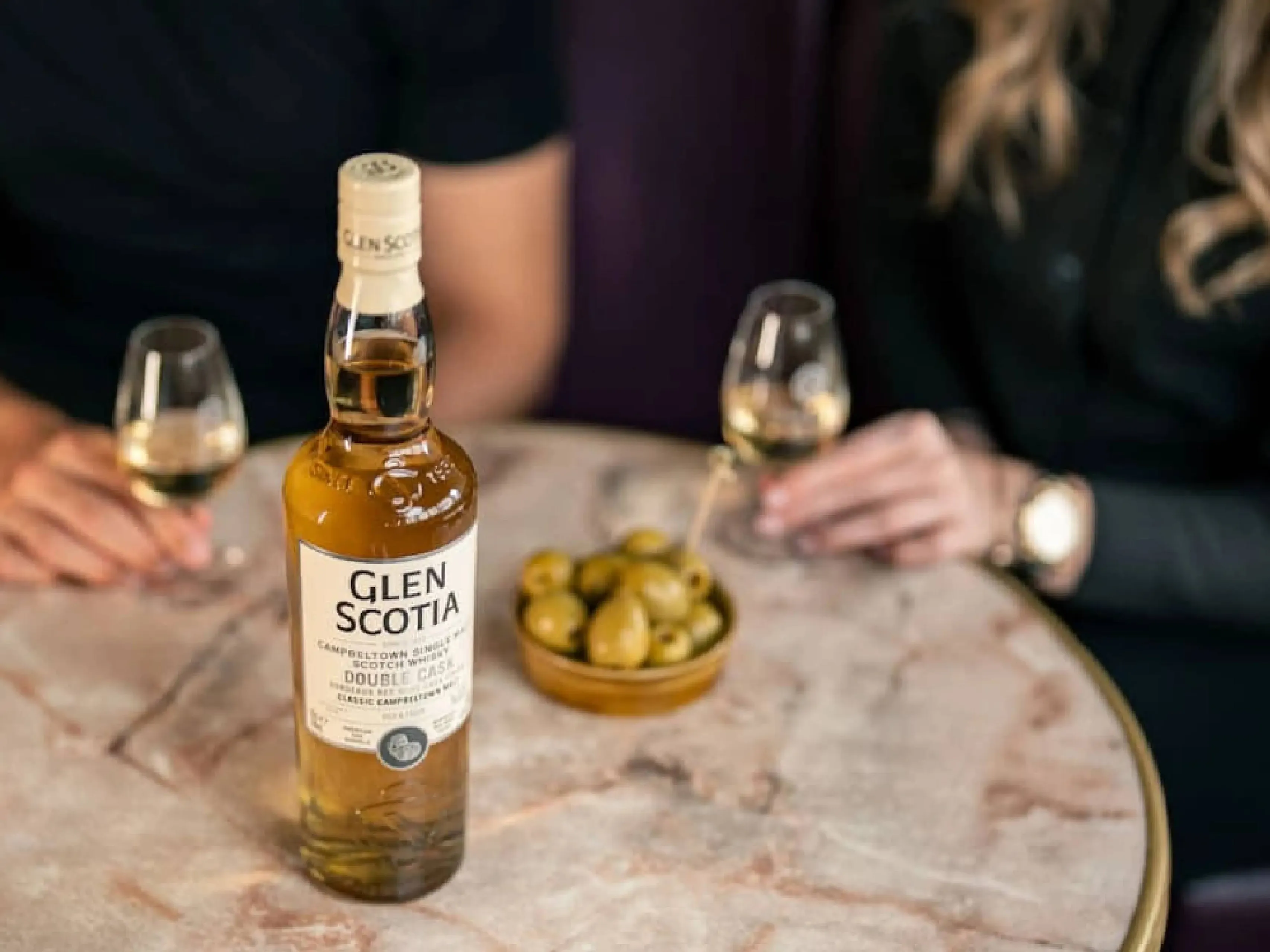 Glen Scotia Double Cask Bordeaux Wine Finish whiosky  op tafel bij vrouwen met glas erbij