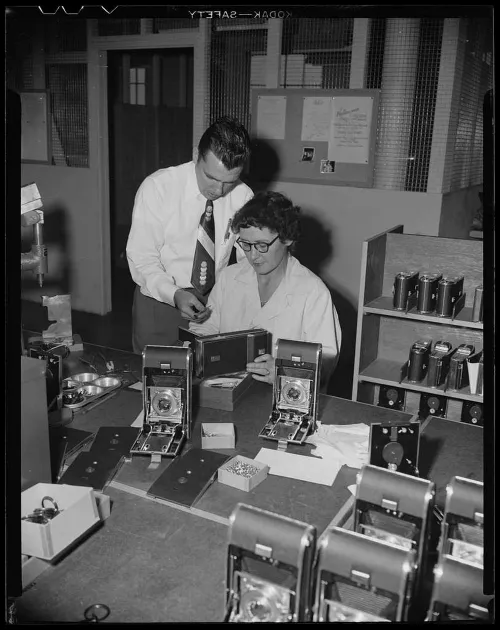 picryl cc a man leans over a woman working on a polaroid camera d3d362