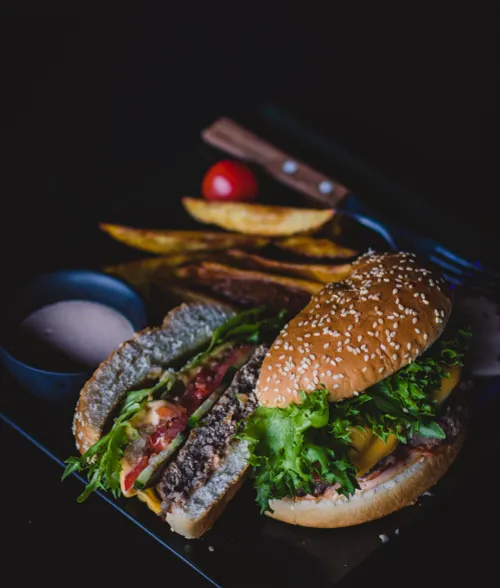 canva burger with green leafy vegetable and cheese on black plate