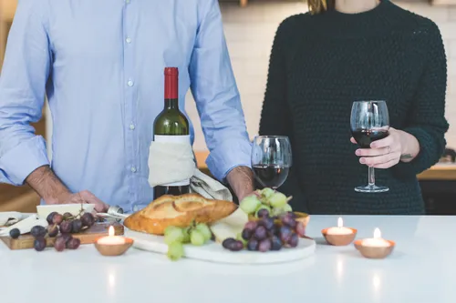 canva man standing beside woman holding wine glass in front of grapes and bread on table