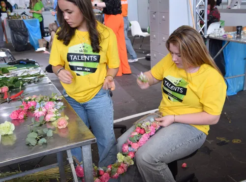 Enola is bezig met het maken van de guirlande. De meiden werken goed samen, Nylah zorgt ervoor dat de bloemen klaarliggen om verwerkt te worden.