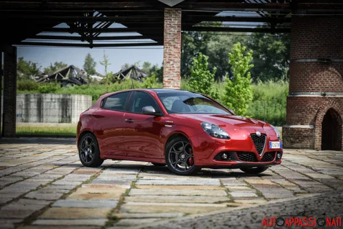 Foto di una Alfa Romeo Giulietta Veloce fotografata di tre quarti anteriore, di colore Rosso Competizione e parcheggiata in una corte.