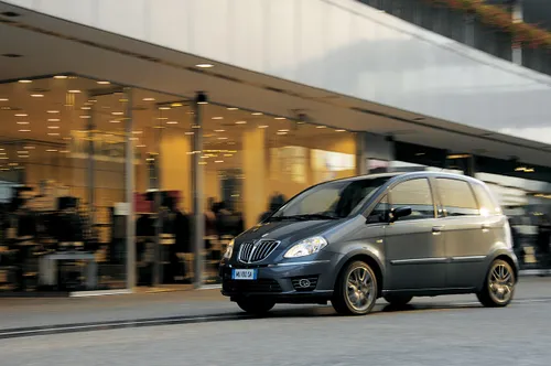 lancia musa di colore grigio che percorre una strada davanti a un palazzo vetrato