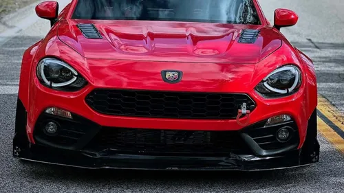 nella foto si vede una 124 spider rossa, sta volta vista da davanti con il muso in primo piano, dove si possono notare i dettagli del kit widebody nero montato sulla macchina