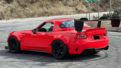 Nella foto si vede una 124 spider rossa di profilo con un alettone nero di grandi dimensioni. La foto è stata scattata in una piazzola di sosta di una strada collinare americana
