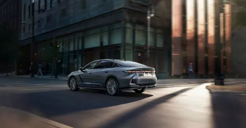 Vista posteriore in movimento della nuova Lexus ES 2026 su strada cittadina: design aerodinamico della carrozzeria e innovativa barra luminosa a LED continua.