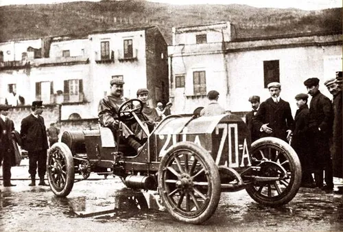 Vincenzo Lancia su una Lancia 20A con lo sfondo di diverse persone e case d'epoca