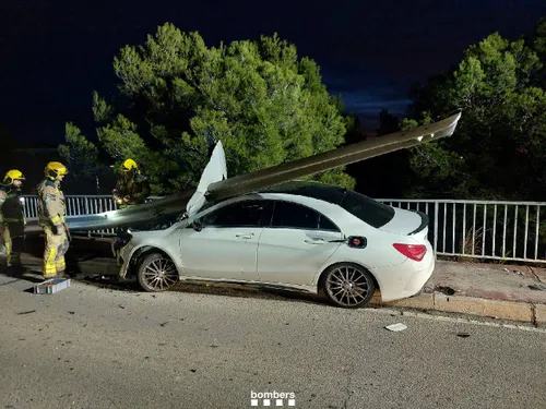 Nell'immagine una macchina incidentata abbia divelto il guardrail e abbia sfondato il cofano senza intaccare il parabrezza. Vicini alla vettura si vedono due vigili del fuoco che lavorano per sistemare la situazione.