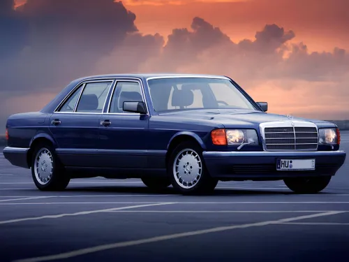 La foto ritrae una Mercedes W126 nera davanti ad un tramonto coperto dalle nuvole