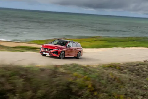 Una foto dinamica della Peugeot 308 SW 2026 di colore rosso che percorre una strada statale del Portogallo sul lungomare