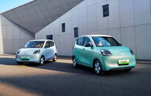 Due Wuling Mini EV parcheggiate davanti a un edificio moderno geometrico. A sinistra l'auto è azzurra, a destra è verde menta con tetto bianco. Entrambe mostrano il design squadrato e compatto tipico di questa popolare city car elettrica cinese.