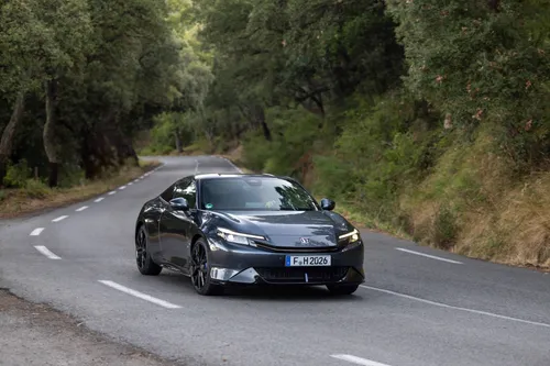 Una foto della Honda Prelude Hybrid 2026 e:HEV impegnata in una curva a sinistra, verniciata in grigio e in mezzo ad una strada di campagna