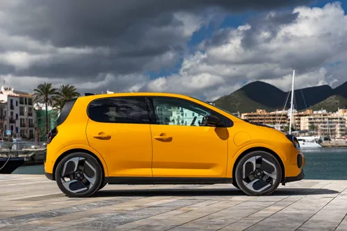 La vista laterale della Renault Twingo 2026 IV E-Tech verniciata in Giallo Mango, cerchi da 18 pollici diamantati e fotografata nel porto di Ibiza
