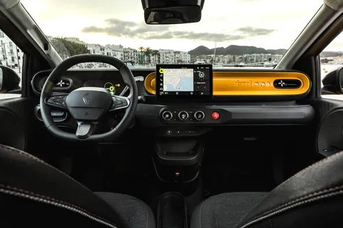 Una foto intera della plancia della Renault Twingo 2026 IV E-Tech con dettagli in giallo mango e, sullo sfondo, la città di Ibiza