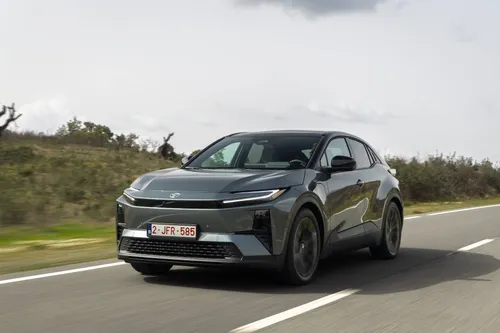 Il frontale della Toyota C-HR+ 2026 grigia metallizzata che percorre una strada extraurbana rettilinea con targa Belga