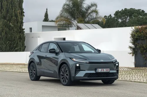 Foto del frontale della Toyota C-HR+ 2026, posizionata di tre quarti anteriore, con una casa moderna come sfondo