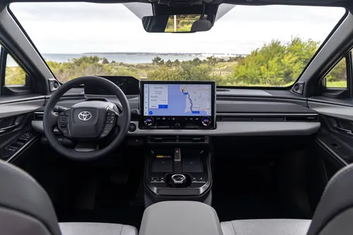 Foto degli interni della Toyota C-HR+ 2026, con rivestimenti grigio chiaro, con un paesaggio marittimo che si vede attraverso il parabrezza