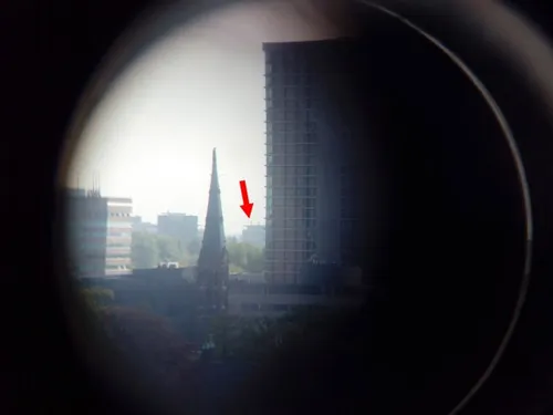 Zicht vanaf Flux door een verrekijker. De rode pijl geeft de positie aan van de andere optische antenne op het dak van gebouw 37 van de High Tech Campus.