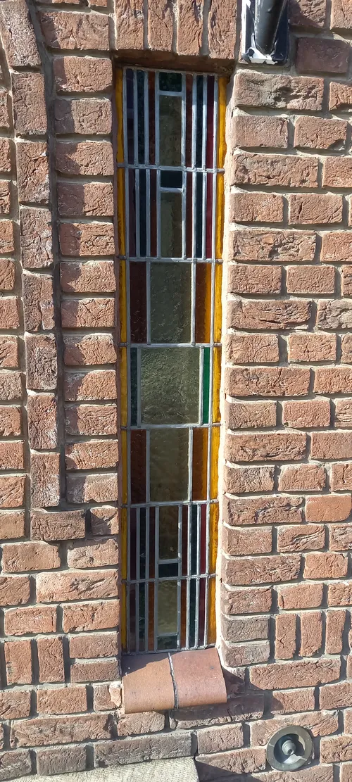 Het glas-in-loodraam is geplaatst in een muur van hardgrauw bakstenen met verdiepte voegen