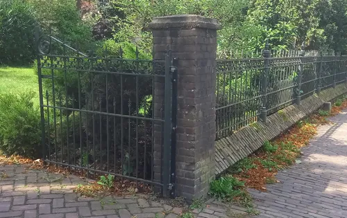 De tuinafscheiding is een lage muur met ezelsrug en daarop een smeedijzeren hekwerk