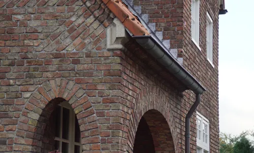Detail van het metselwerk rondom de portiek op de hoek van de noord- en westgevel. Onder de gevelpan is de profilering in de steen en het ornament te zien