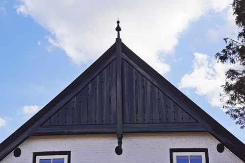 De gevelmakelaar is de verticale middenstijl, welke aan de boven- en onderzijde een versiering heeft. De middenstijl staat tussen de twee windveren en over de horizontale trek[plaat.