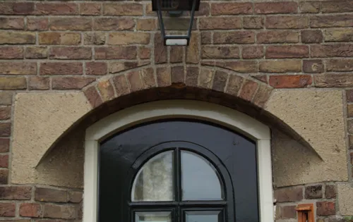 De voordeur met een segmentboog aan de bovenzijde bevindt zich in een schuine nis