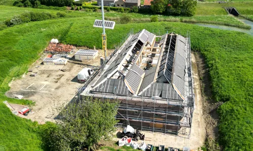 De dakplaten voor de nieuwe schilddaken worden op de gordingen van de staalconstructie gelegd. De bijbouwsels op het terreplein zijn inmiddels verwijderd. Rechtsboven ligt de inundatiesluis, het Oude Maasje en de Hoge Maasdijk.