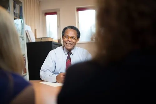 Standaardfoto bij BIJSCHRIFT column WEL Uitsnijden Harry vriendelijk lachend aan bureau in gesprek met twee patiënten. Ook homepagefoto_JGS7931