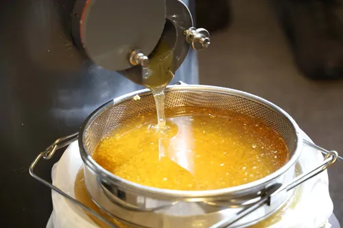 De honing uit de honingslinger wordt opgevangen in een zeef die op een emmer rust