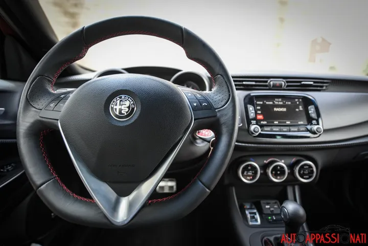 Foto degli interni di una Alfa Romeo Giulietta Veloce, con focus sul volante sportivo e gli interni neri.