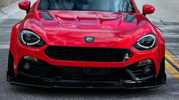 nella foto si vede una 124 spider rossa, sta volta vista da davanti con il muso in primo piano, dove si possono notare i dettagli del kit widebody nero montato sulla macchina