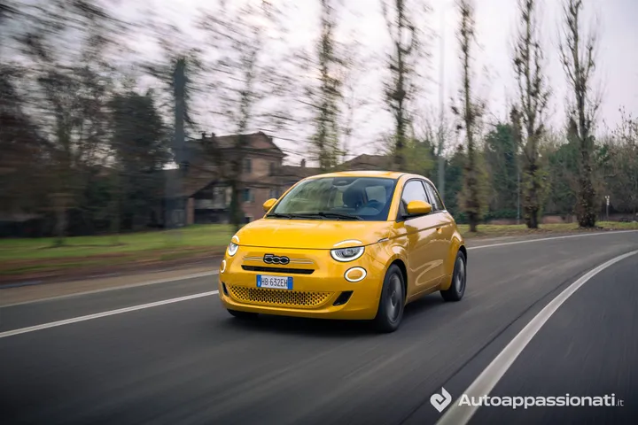 Foto dinamica anteriore della FIAT 500 Hybrid su strada asfaltata con alberi sullo sfondo