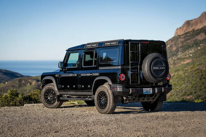 La Ineos Grenadier del 2026 nella versione black edition di colore nero con sfondo delle montagne e nella vista posteriore