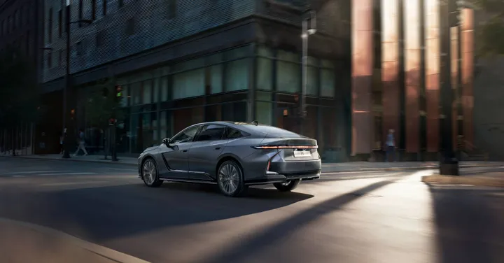 Vista posteriore in movimento della nuova Lexus ES 2026 su strada cittadina: design aerodinamico della carrozzeria e innovativa barra luminosa a LED continua.