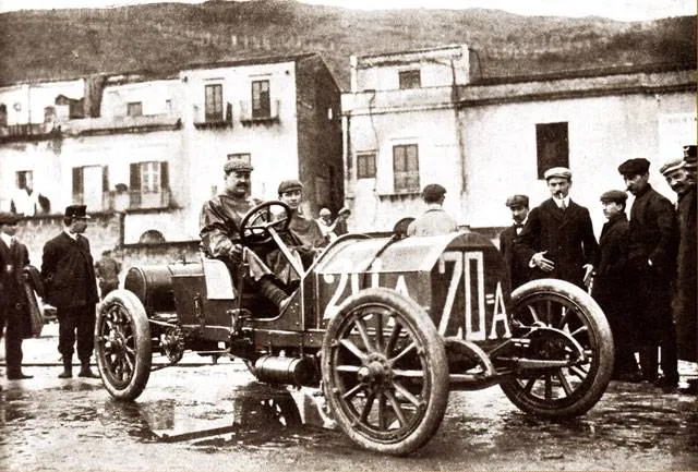 Vincenzo Lancia su una Lancia 20A con lo sfondo di diverse persone e case d'epoca