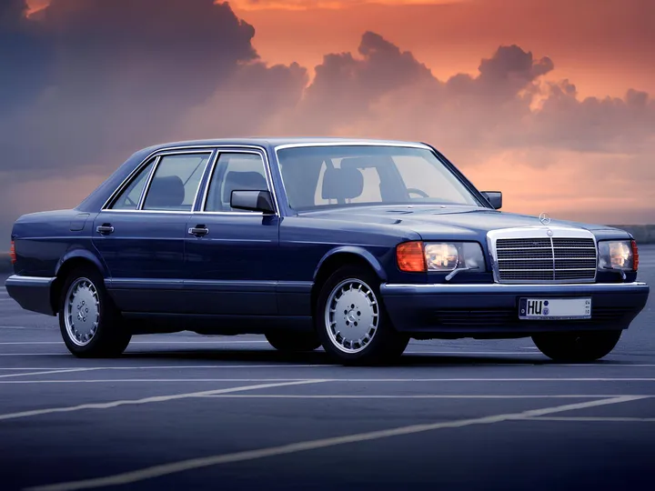 La foto ritrae una Mercedes W126 nera davanti ad un tramonto coperto dalle nuvole