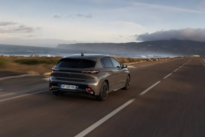 Una foto della Peugeot 308 2026 dinamica nel lato posteriore che percorre una strada costiera del Portogallo