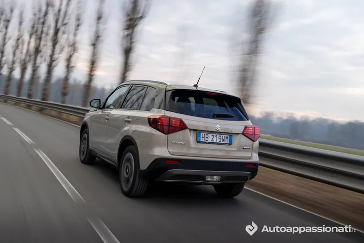 Foto posteriore della Suzuki Vitara Hybrid AllGrip dal lato posteriore, su una strada extraurbana con alberi&nbsp;